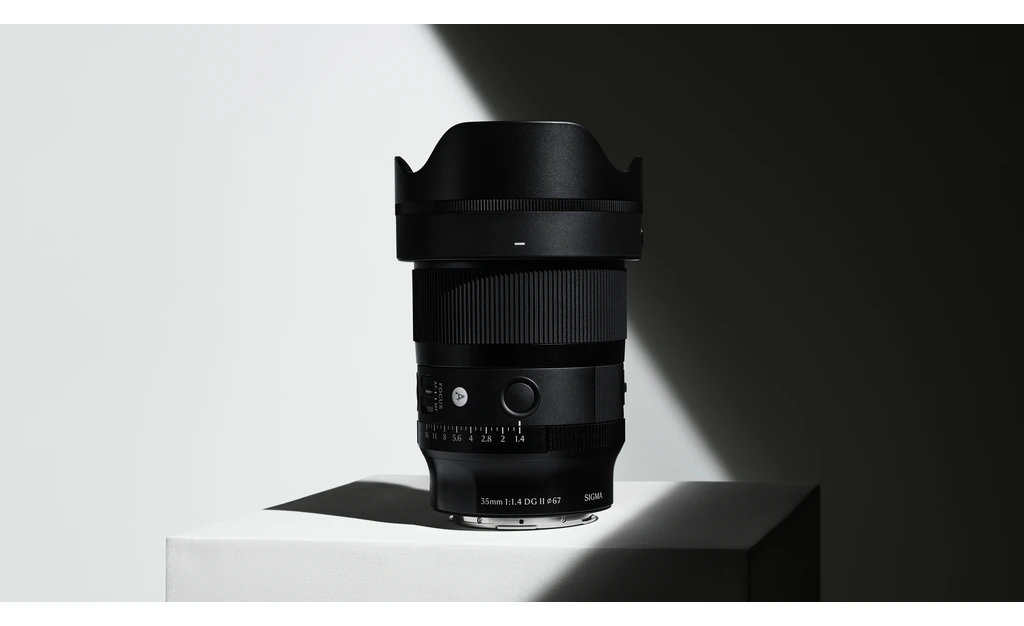لنز سیگما Sigma 35mm F1.4 DG II مانت Sony E 1 لنز سیگما 35mm F1.4 DG II با هود پاپتی نصبشده، ایستاده روی سطح سفید
